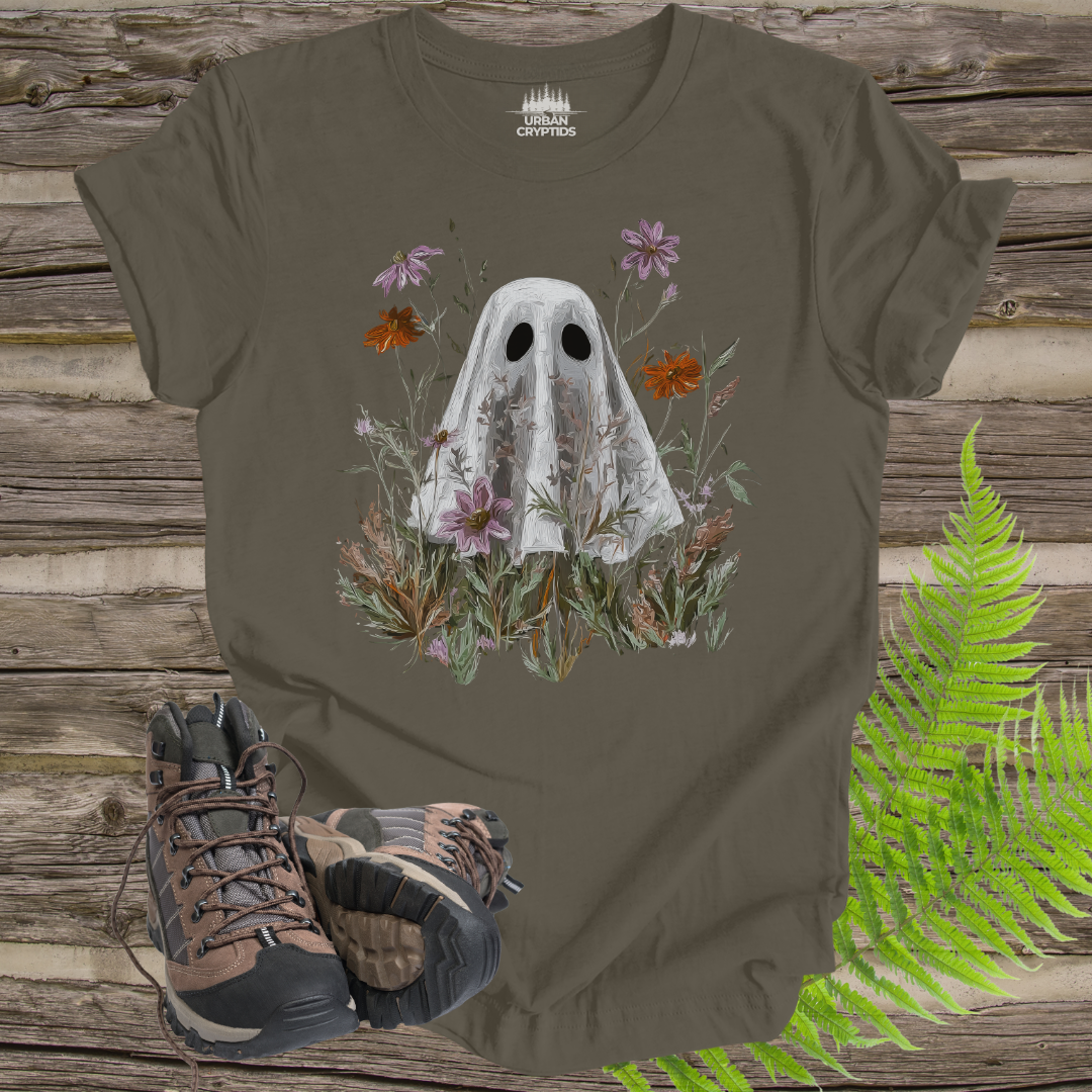T-shirt with ghost and floral design on a wooden surface with hiking boots and ferns.