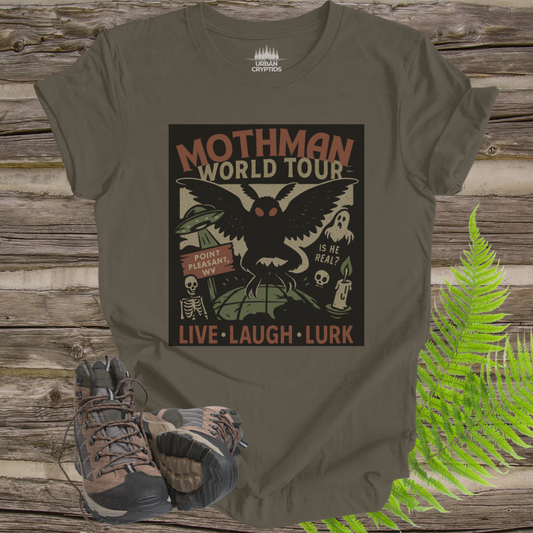 Green t-shirt with Mothman graphic design on a wooden surface with hiking boots and ferns.