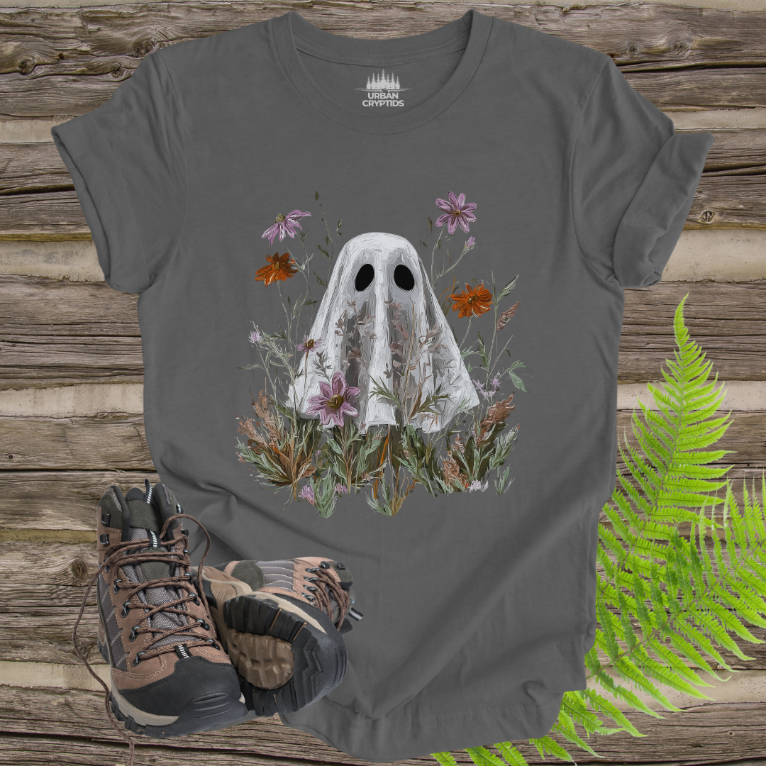 Gray t-shirt with ghost and floral design on a wooden surface with hiking boots and ferns.
