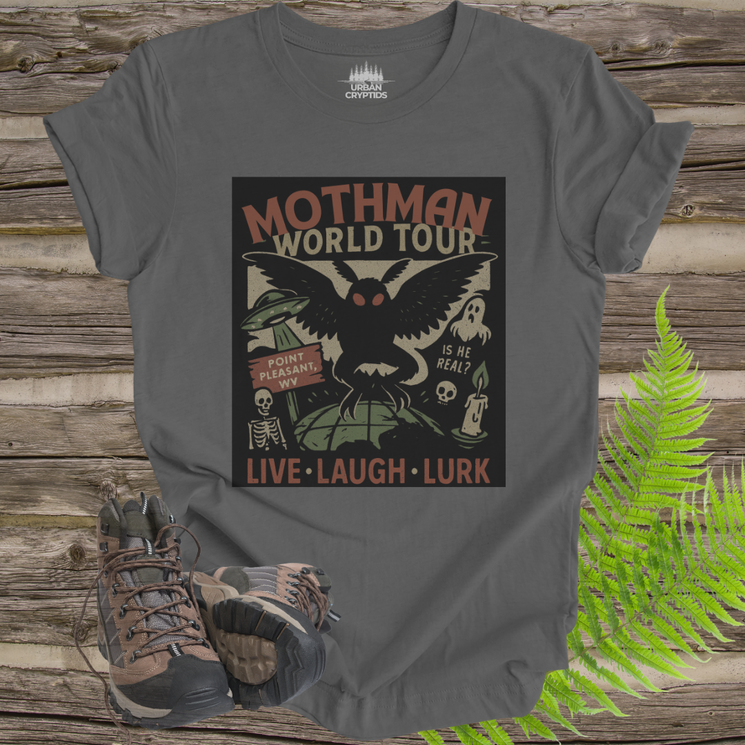Gray t-shirt with Mothman graphic design on a wooden surface with hiking boots and ferns.