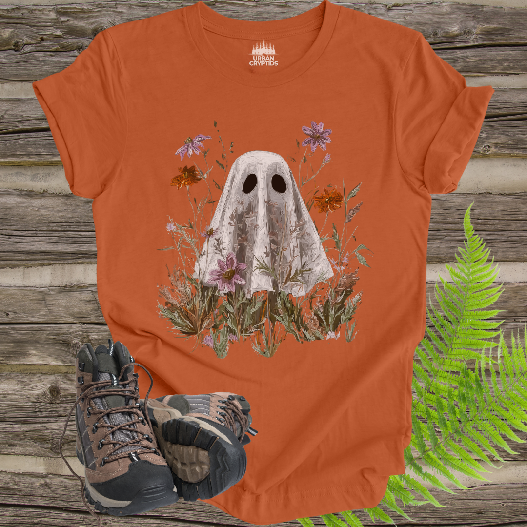 Orange t-shirt with ghost and floral design on a wooden surface with hiking boots and ferns.