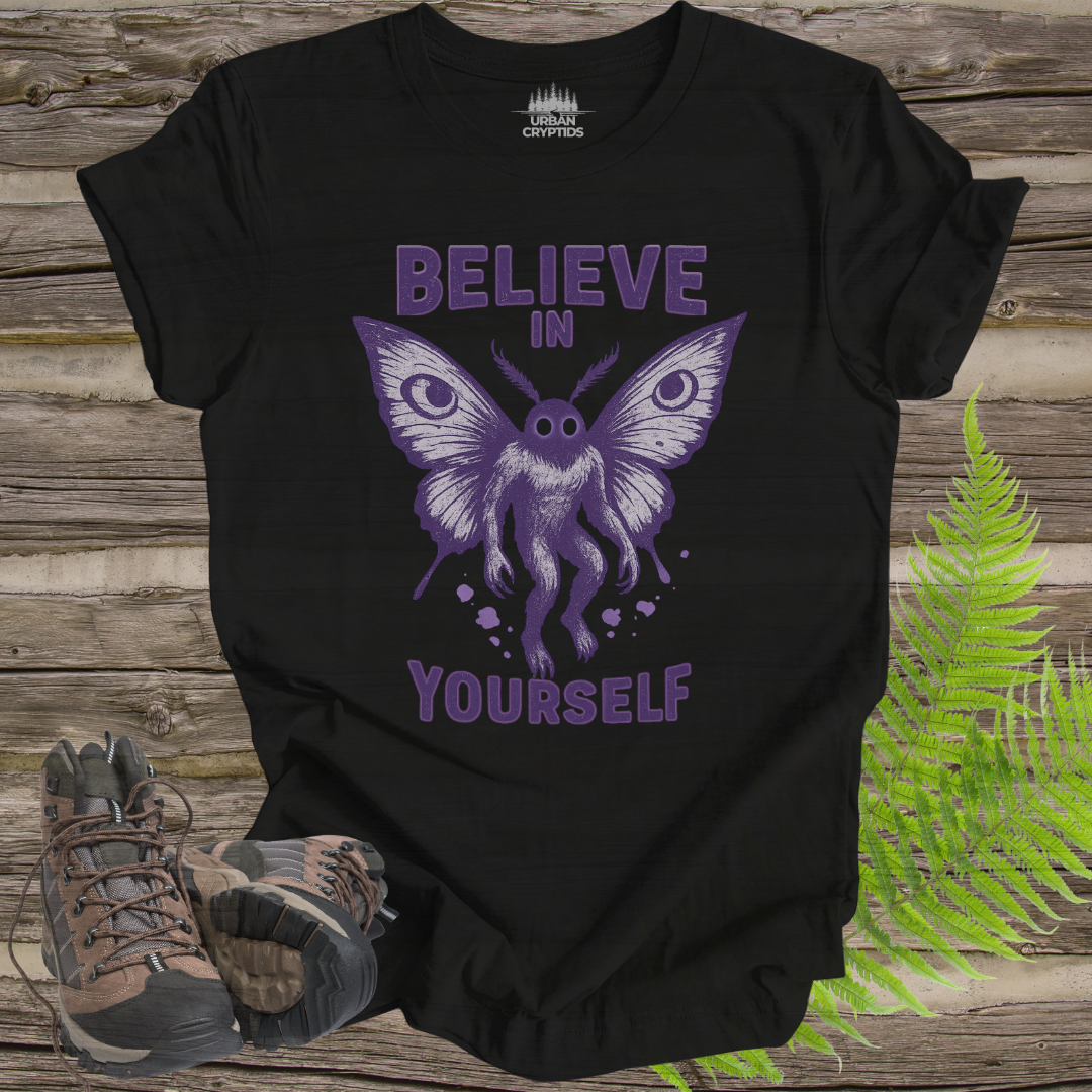 Black t-shirt with purple butterfly graphic and 'Believe in Yourself' text on a wooden surface with hiking boots and ferns.