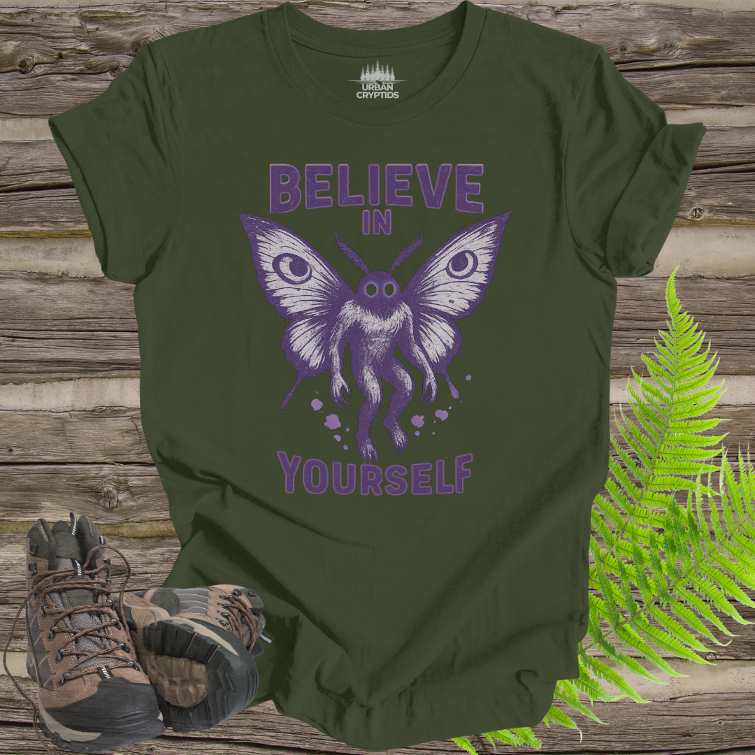 Green t-shirt with purple butterfly graphic and 'Believe in Yourself' text on a wooden surface with boots and fern.