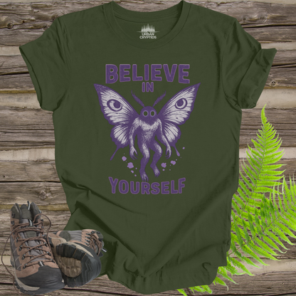 Green t-shirt with purple butterfly graphic and 'Believe in Yourself' text on a wooden surface with boots and fern.