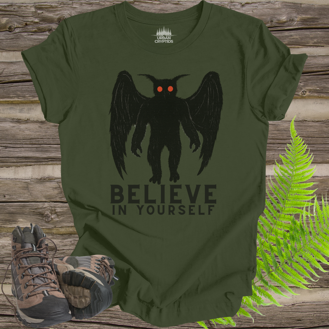 Green t-shirt with a black creature graphic and 'BELIEVE IN YOURSELF' text on a wooden background.