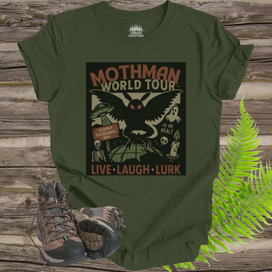 Green t-shirt with Mothman graphic design on a wooden surface with hiking boots and fern.