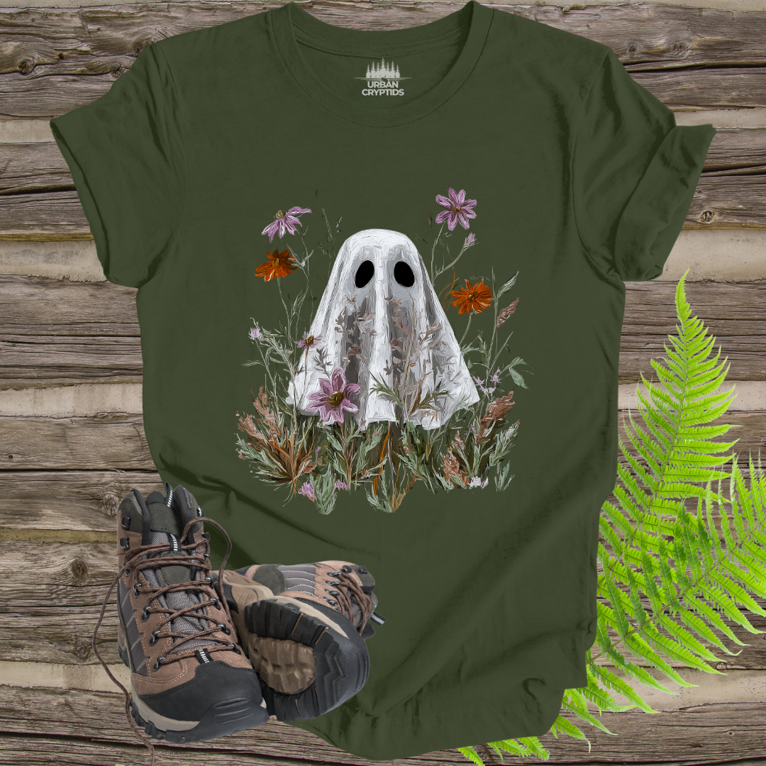 Green t-shirt with ghost and floral design on a wooden surface with hiking boots and ferns.